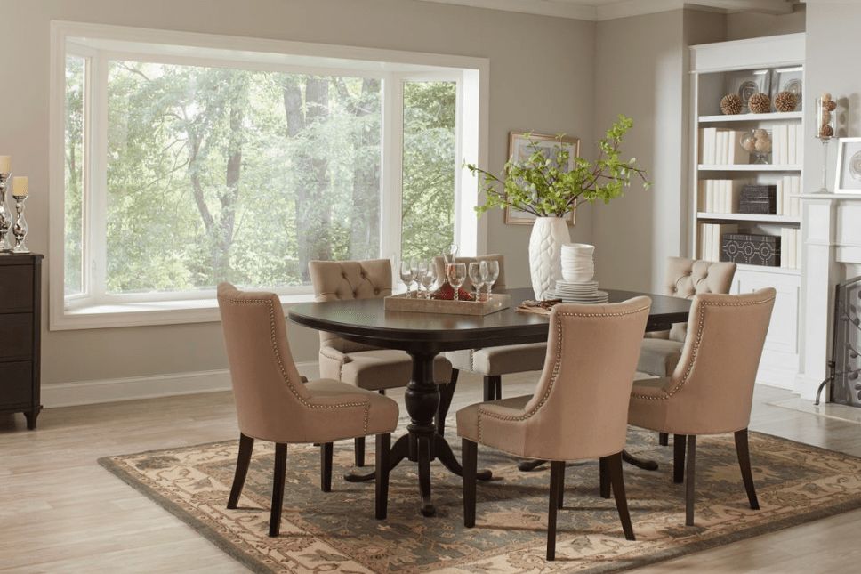 A furnished dining room with a three-panel bay window and woods visible outside.