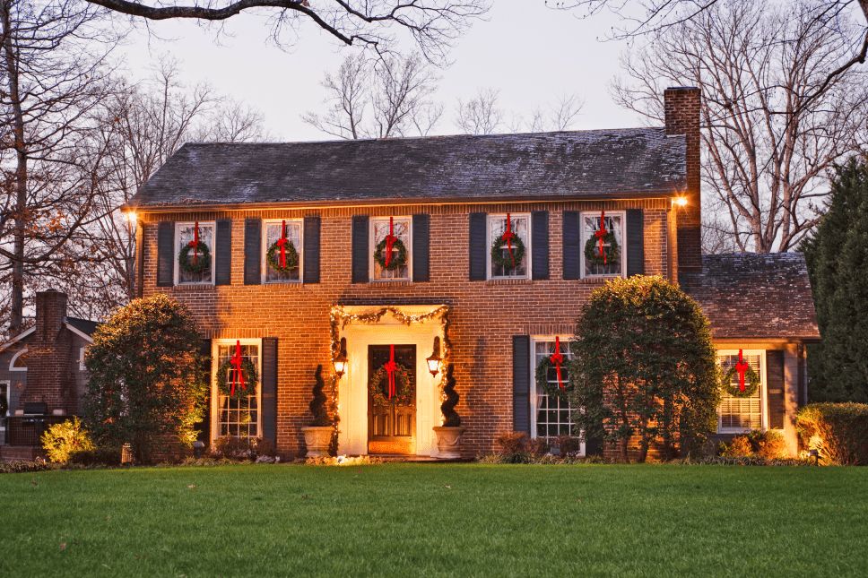 A brick house with multiple wreaths hanging in the windows using ribbons.