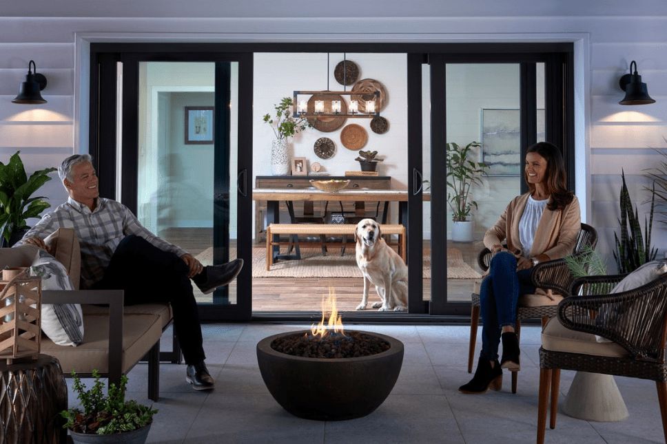 A couple sitting on outdoor furniture at dusk with a large sliding patio door behind them.