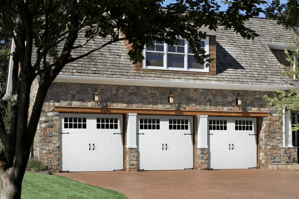Three white garage doors on a home with a stone veneer.