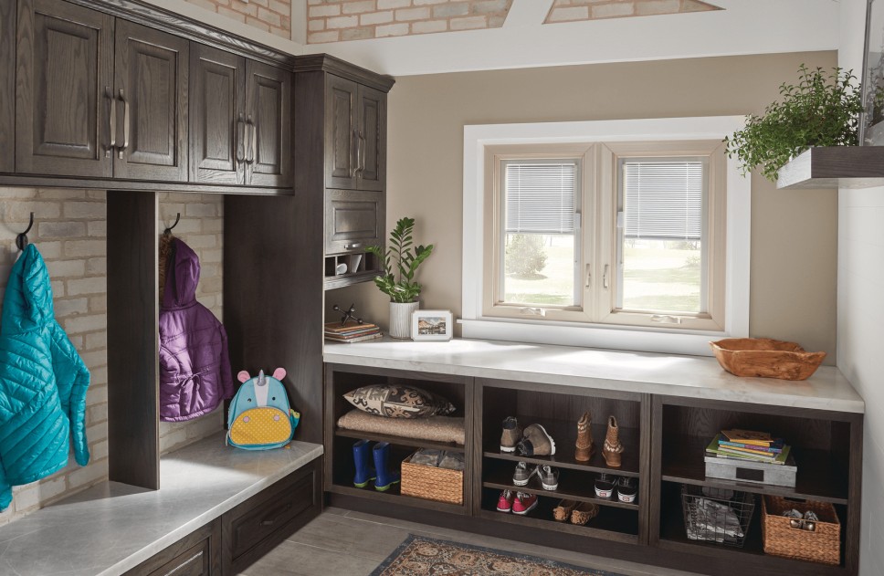 A naturally lit mudroom containing wooden cabinetry, countertops, a large window, and design decor