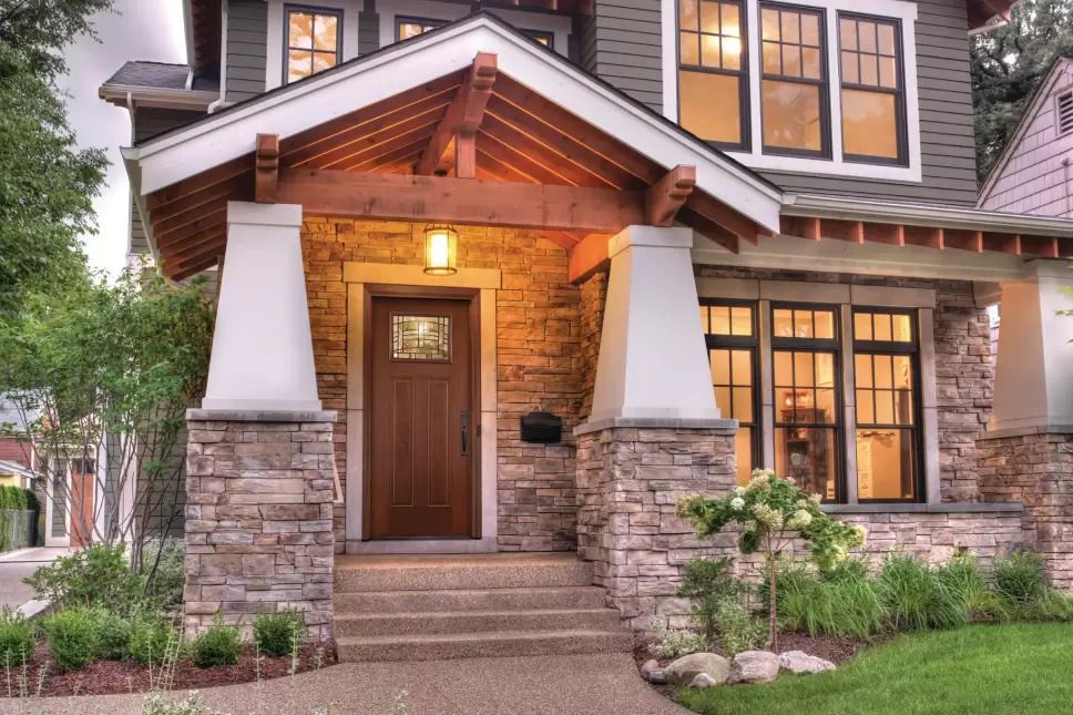 Front porch of a home with black windows with grids and a woodgrain entry door.